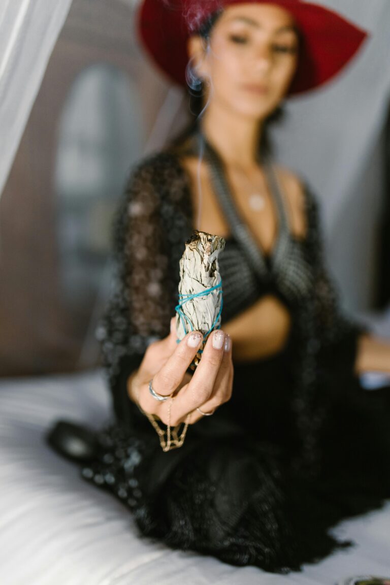 A woman in mystical attire holding sage for a ritual indoors.